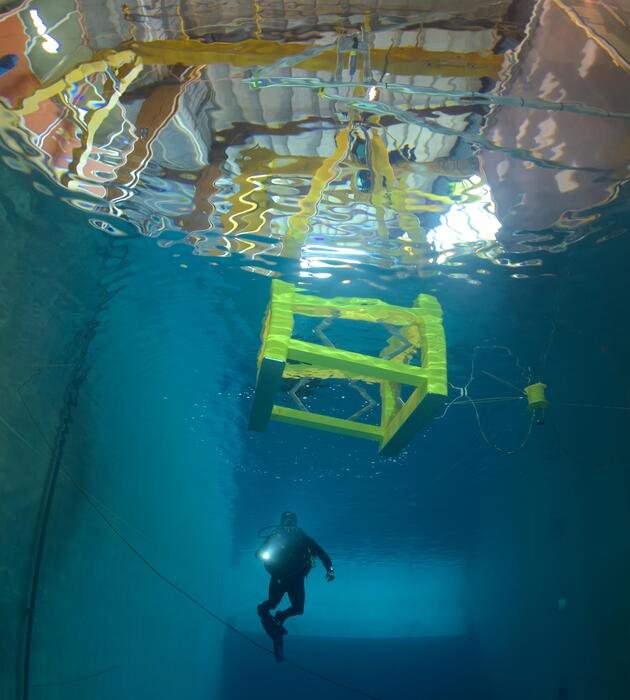 Plongeur sous un prototype d'éolienne flottante dans un bassin d'essais, prise de vue sous l'eau.