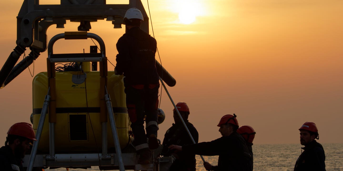 Personnes travaillant sur l'engin sous-marin devant un coucher de soleil.