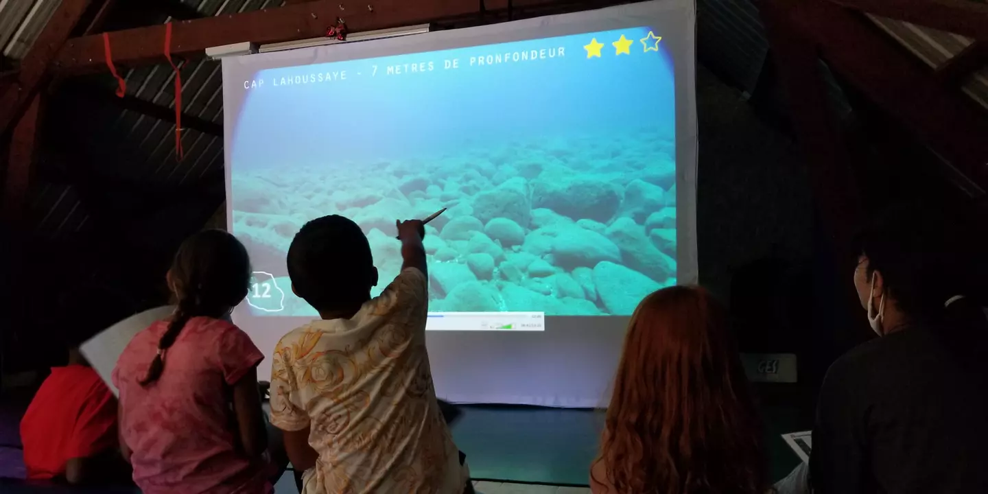 Enfants devant une vidéo projetée sur un écran blanc.