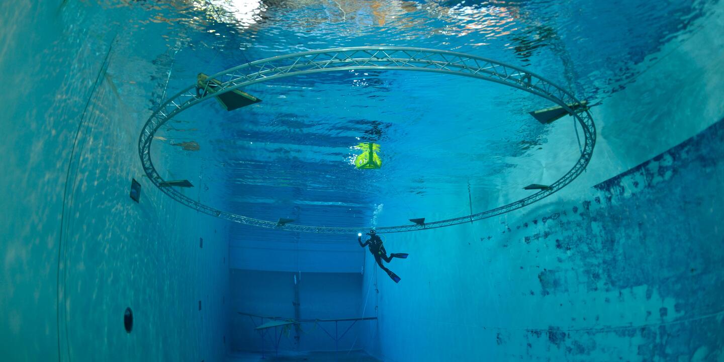 Plongeur dans un bassin d'essais au centre d'une armature circulaire en fer.