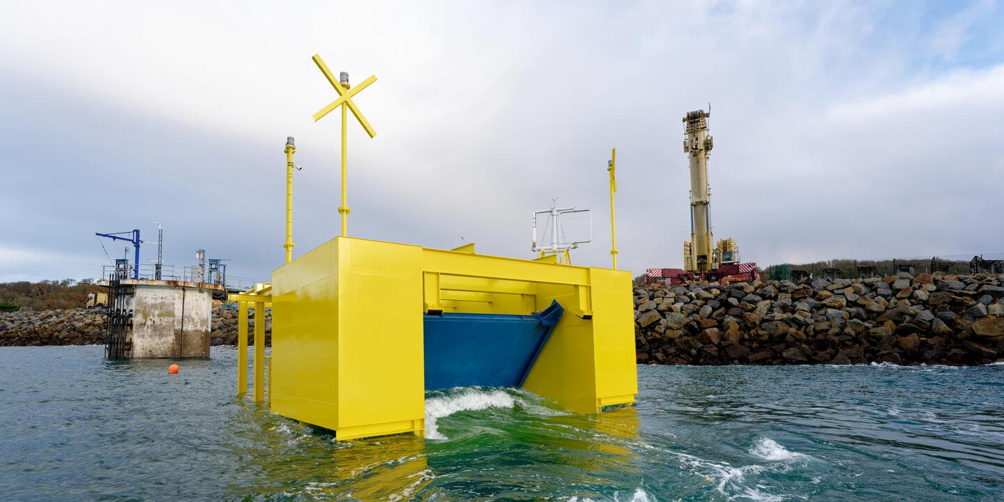Cube jaune placé sur la mer avec un système de porte bleue mobile. Élément placé devant une digue de port.