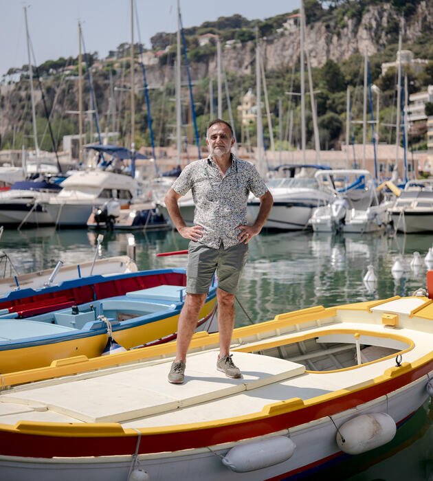 Homme debout sur une barque amarrée dans un port de plaisance. 