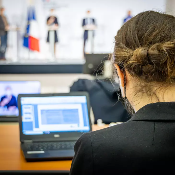 Personne de dos assise avec une conférence en arrière plan.